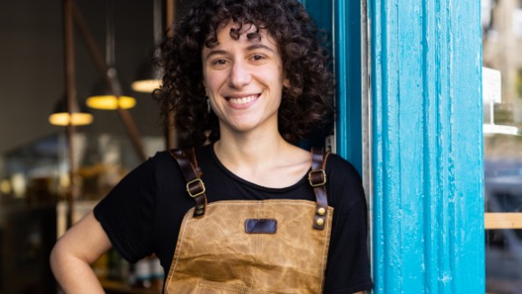 Kvinde med forklæde smiler til kamera på cafe