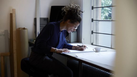 Kvinde_tegner_ved_arbejdsbord_article-card_576x324