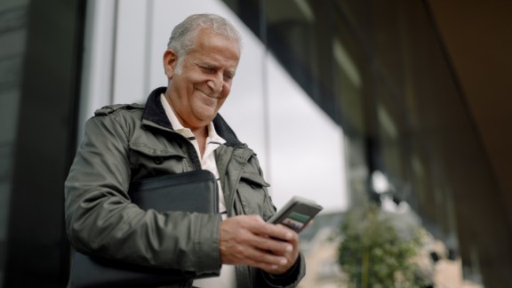 Mand smiler med telefon foran bygning