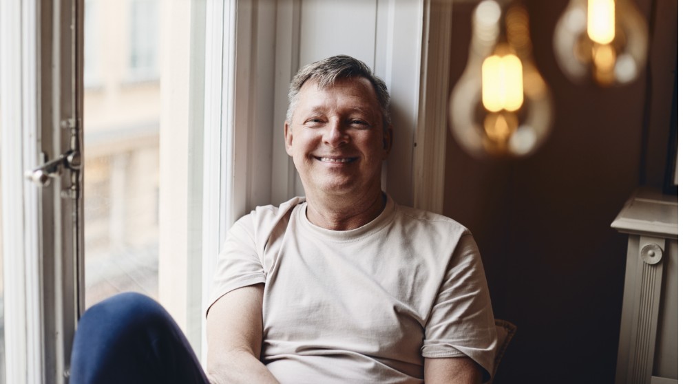 Mand sidder i vindueskarm og smiler til kamera