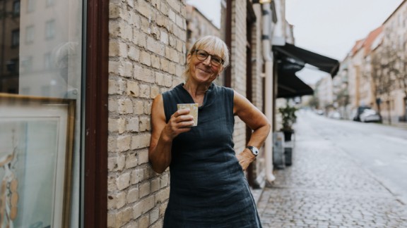 Kvinde smiler og drikker kaffe på gågade