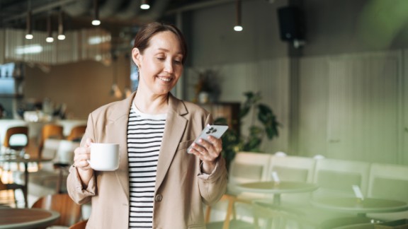 Kvinde kigger på mobil med en kop kaffe i hånden på restaurant