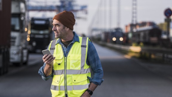 Mand i gul vest taler i telefon med hånden i lommen
