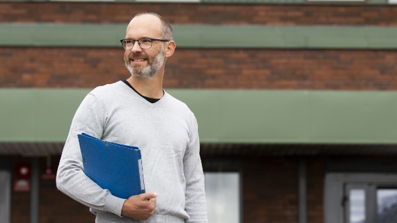 Mand står foran skole med blå mappe i hånden