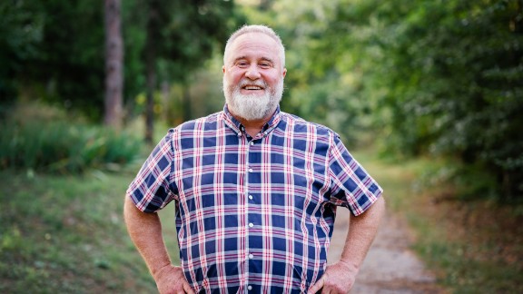 En stor mand står med hænderne på sine hofter, smiler og har en skjorte på