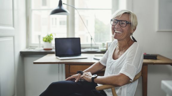 Kvinde_griner_ved_skrivebord_text-image-50_50_576x324