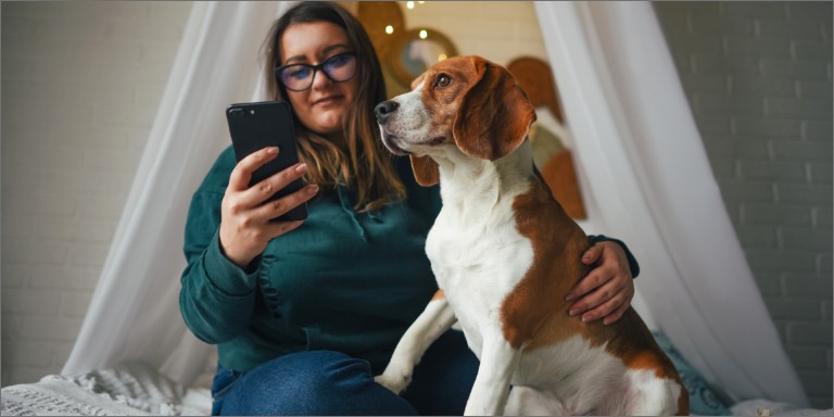 En kvinde kigger på sin mobil og holder sin hund