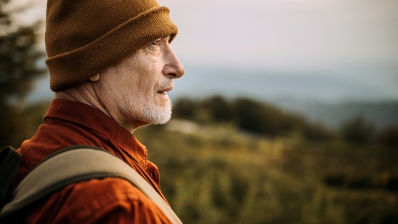 Mand med orange hue og jakke kigger på naturen