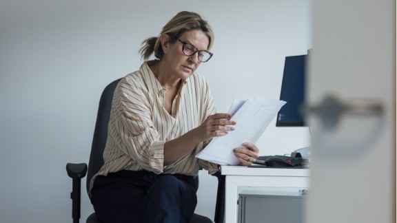 Kvinde sidder på kontorstol og kigger på et stykke papir