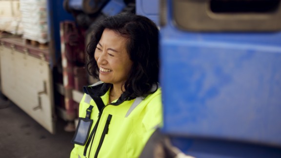 Kvinde med gul vest smiler ved siden af lastbil
