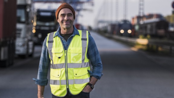 Mand i gul vest med hånden i lommen smiler til kamera