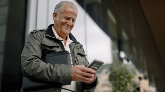 Mand smiler til sin telefon foran bygning