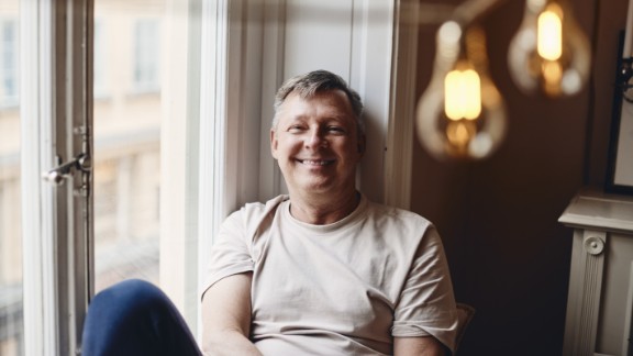 Mand sidder i vindueskarm og smiler til kameraet