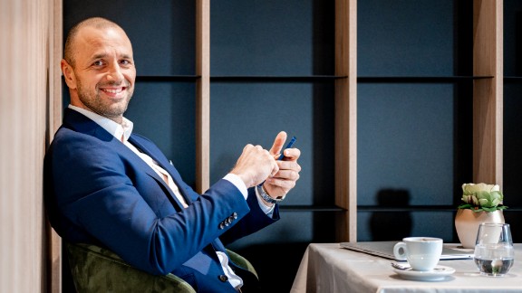 Mand sidder med telefon og kaffekop og smiler