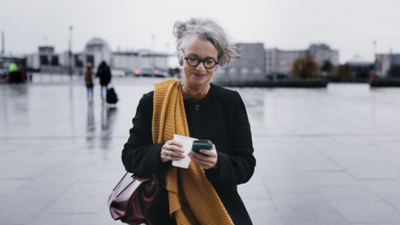 Kvinde med en kop kaffe smiler til sin telefon i by